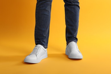 Man wearing stylish white sneakers on yellow background, closeup