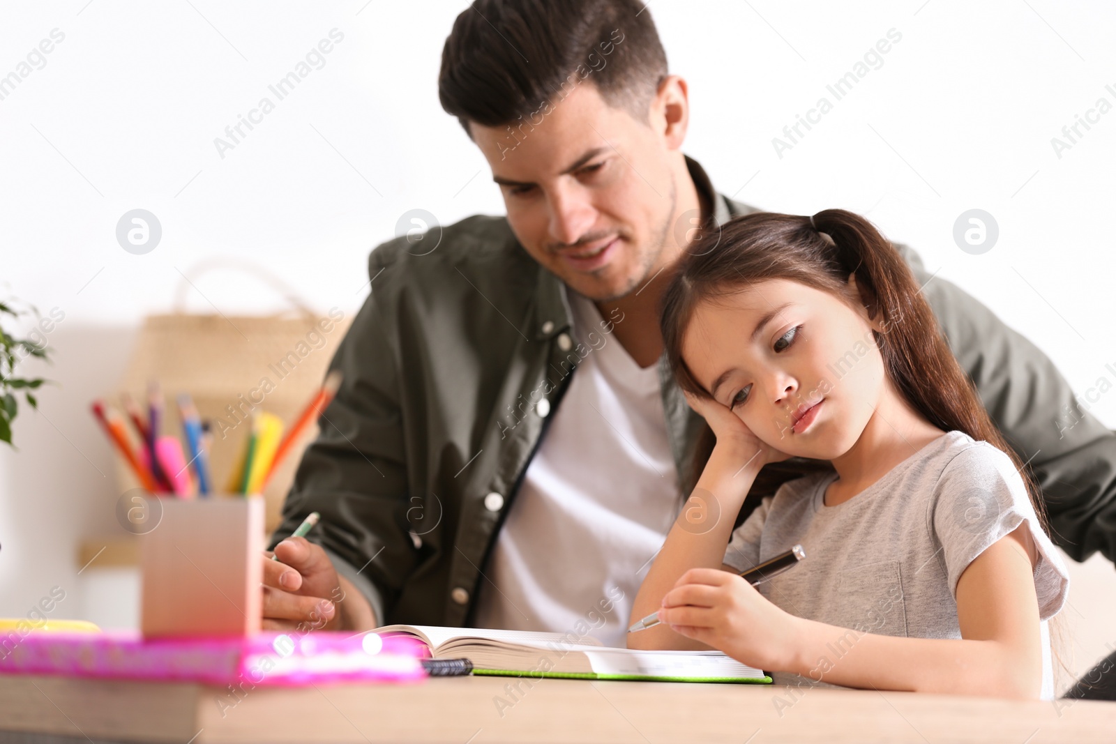 Photo of Man helping his daughter with homework at table indoors