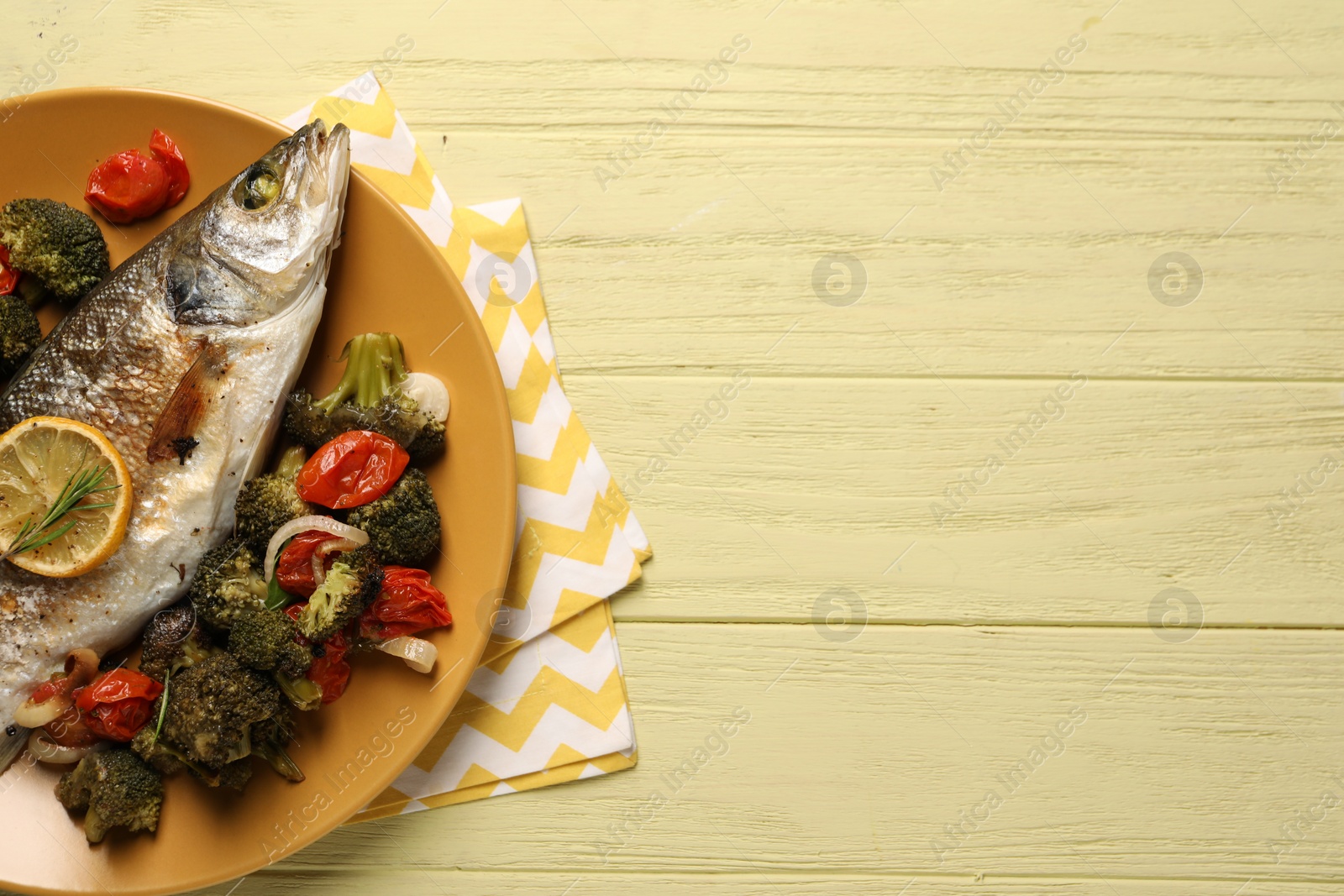 Photo of Delicious baked fish and vegetables on yellow wooden table, top view. Space for text