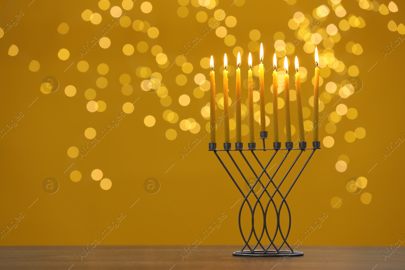 Photo of Hanukkah celebration. Menorah with burning candles on table against yellow background with blurred lights, space for text