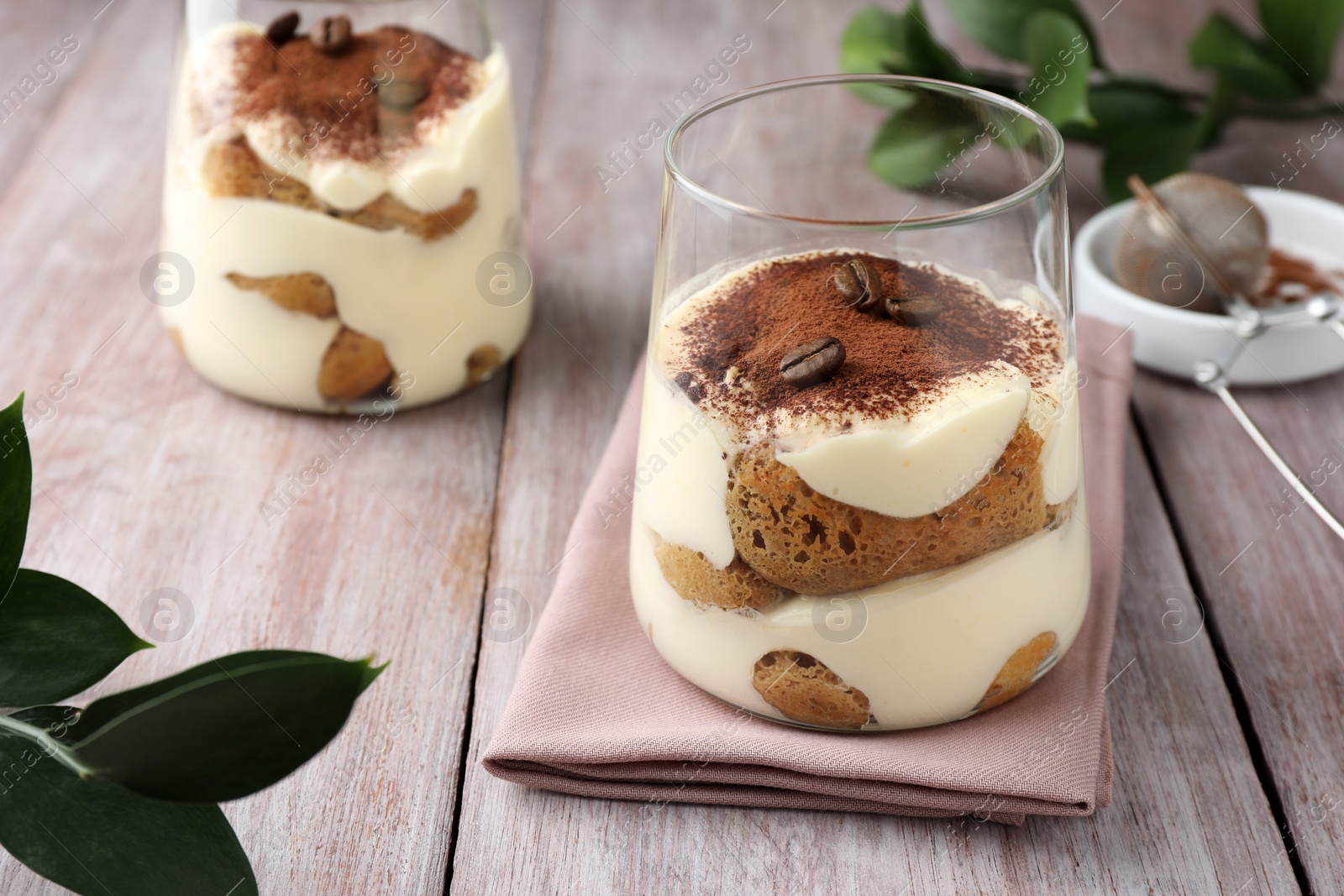 Photo of Delicious tiramisu with coffee beans in glasses and green leaves on wooden table