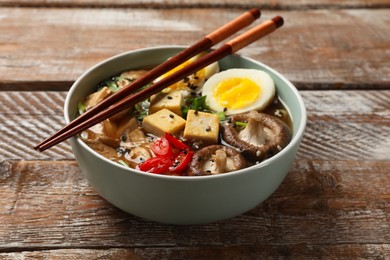 Photo of Bowl of delicious ramen and chopsticks on wooden table. Noodle soup