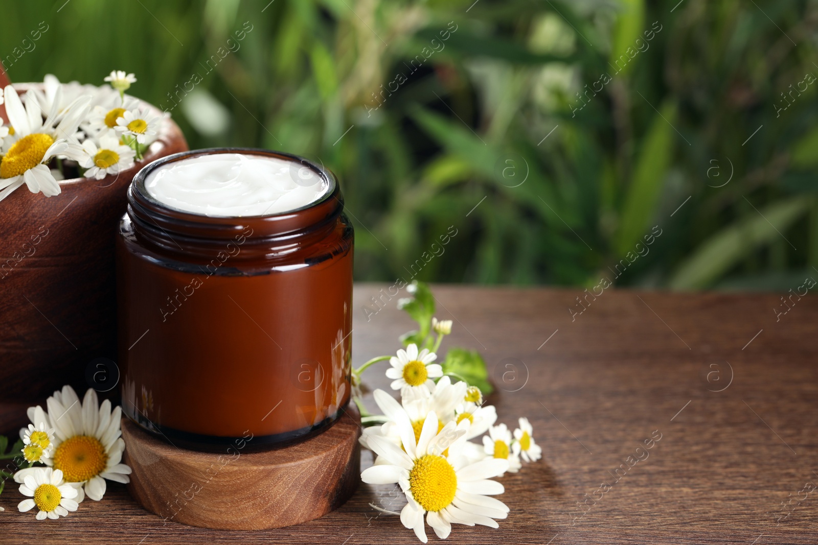 Photo of Jar of hand cream and chamomiles on wooden table, space for text