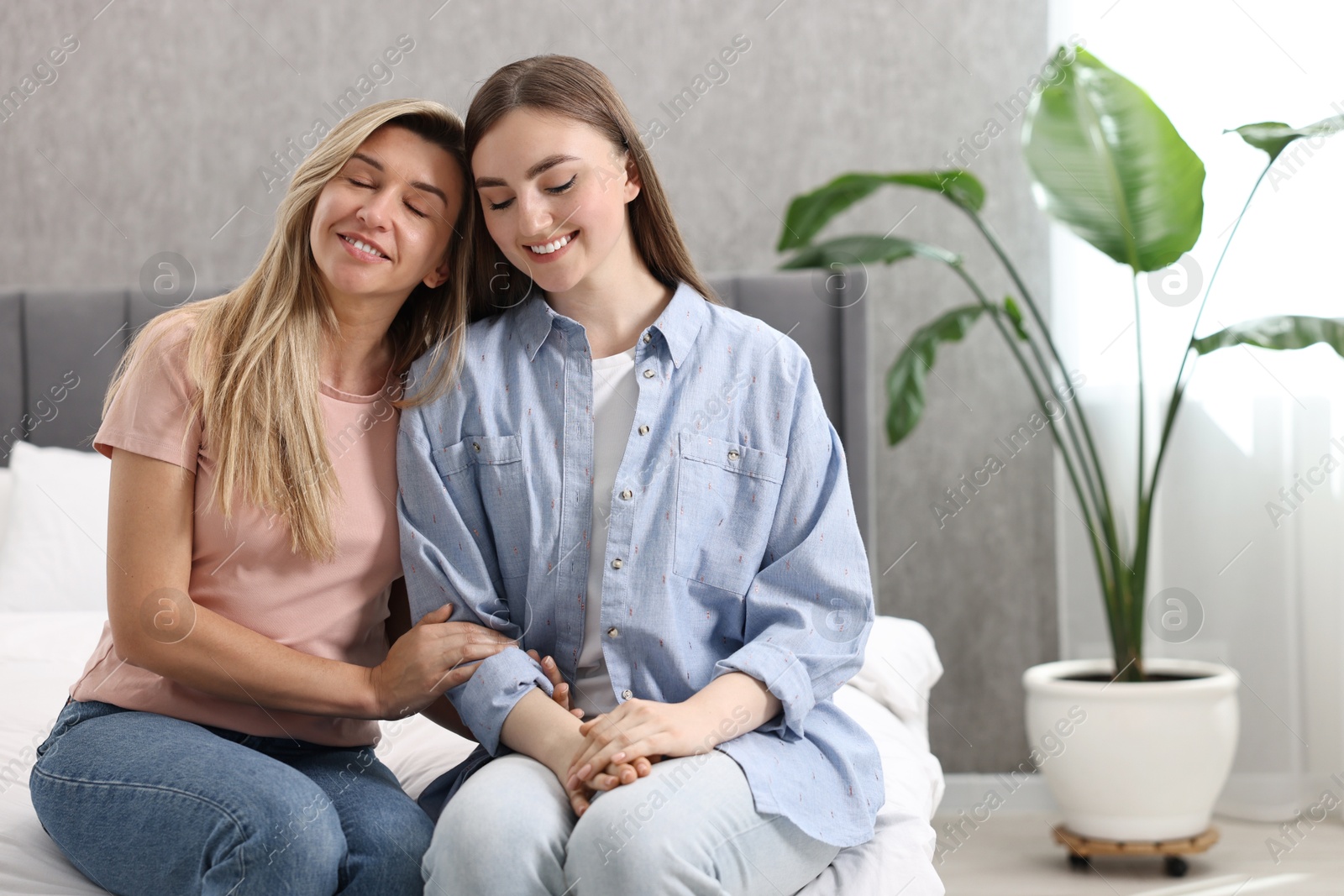 Photo of Happy young women sitting on bed at home, space for text