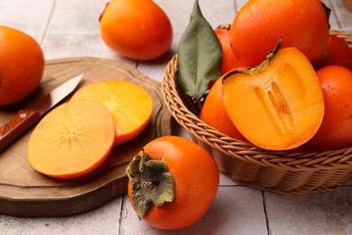 Photo of Delicious ripe juicy persimmons in wicker basket on tiled surface