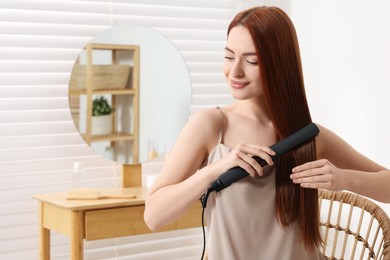 Photo of Beautiful woman using hair iron in room, space for text