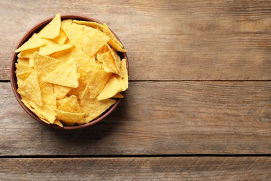 Bowl with tasty tortilla chips (nachos) on wooden table, top view. Space for text