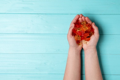 Photo of Woman with colorful jelly bears on wooden background, top view. Space for text