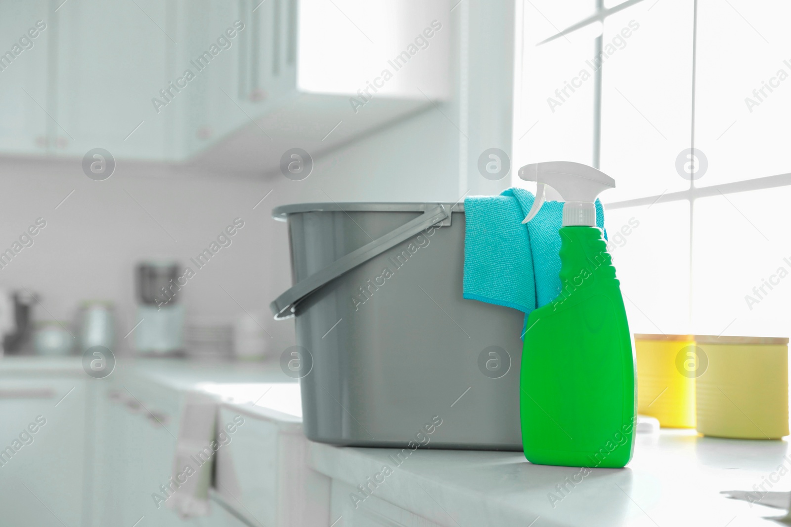 Photo of Detergent and plastic bucket with rag on countertop in kitchen, space for text. Cleaning supplies