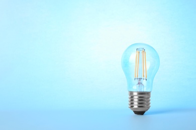 Photo of New modern lamp bulb on light blue background, space for text