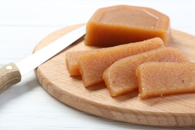 Photo of Tasty sweet quince paste and knife on white wooden table, closeup