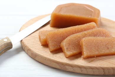 Tasty sweet quince paste and knife on white wooden table, closeup