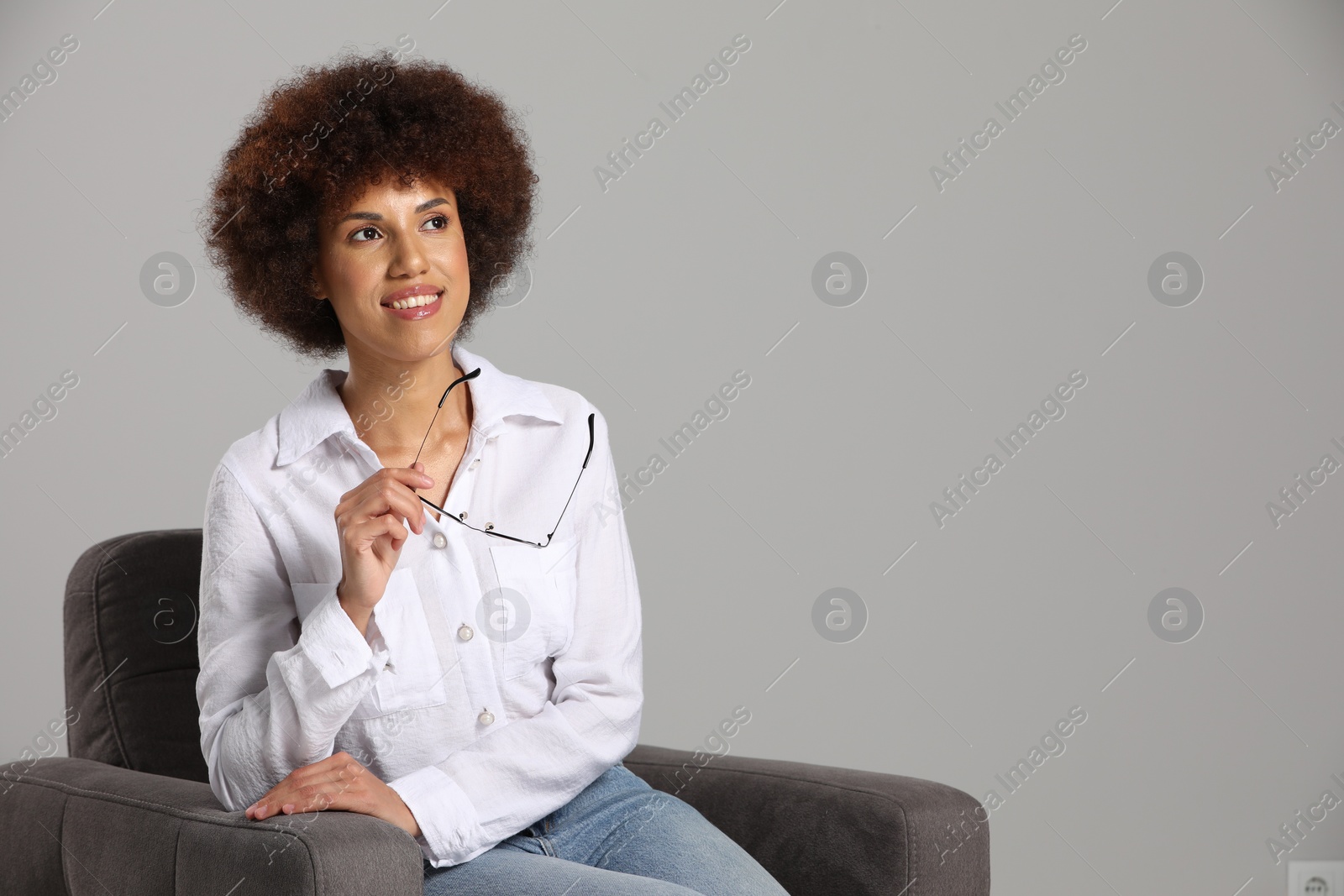 Photo of Beautiful young woman with eyeglasses sitting in armchair on grey background. Space for text