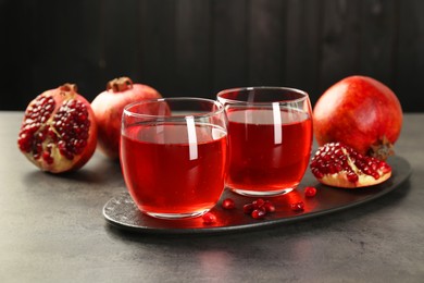Photo of Tasty pomegranate juice in glasses and fresh fruits on grey table