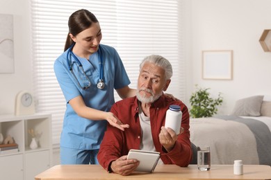 Young healthcare worker consulting senior man at wooden table indoors