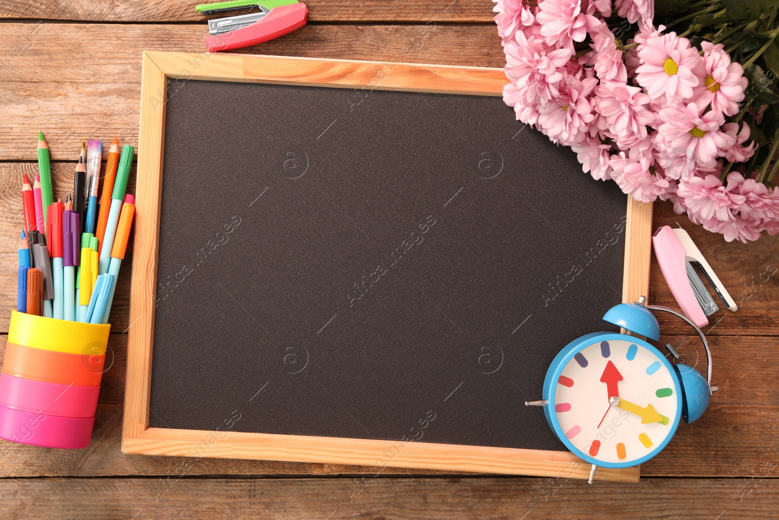 Photo of Blackboard, stationery, alarm clock and flowers on wooden table, flat lay with space for text. Teacher's Day