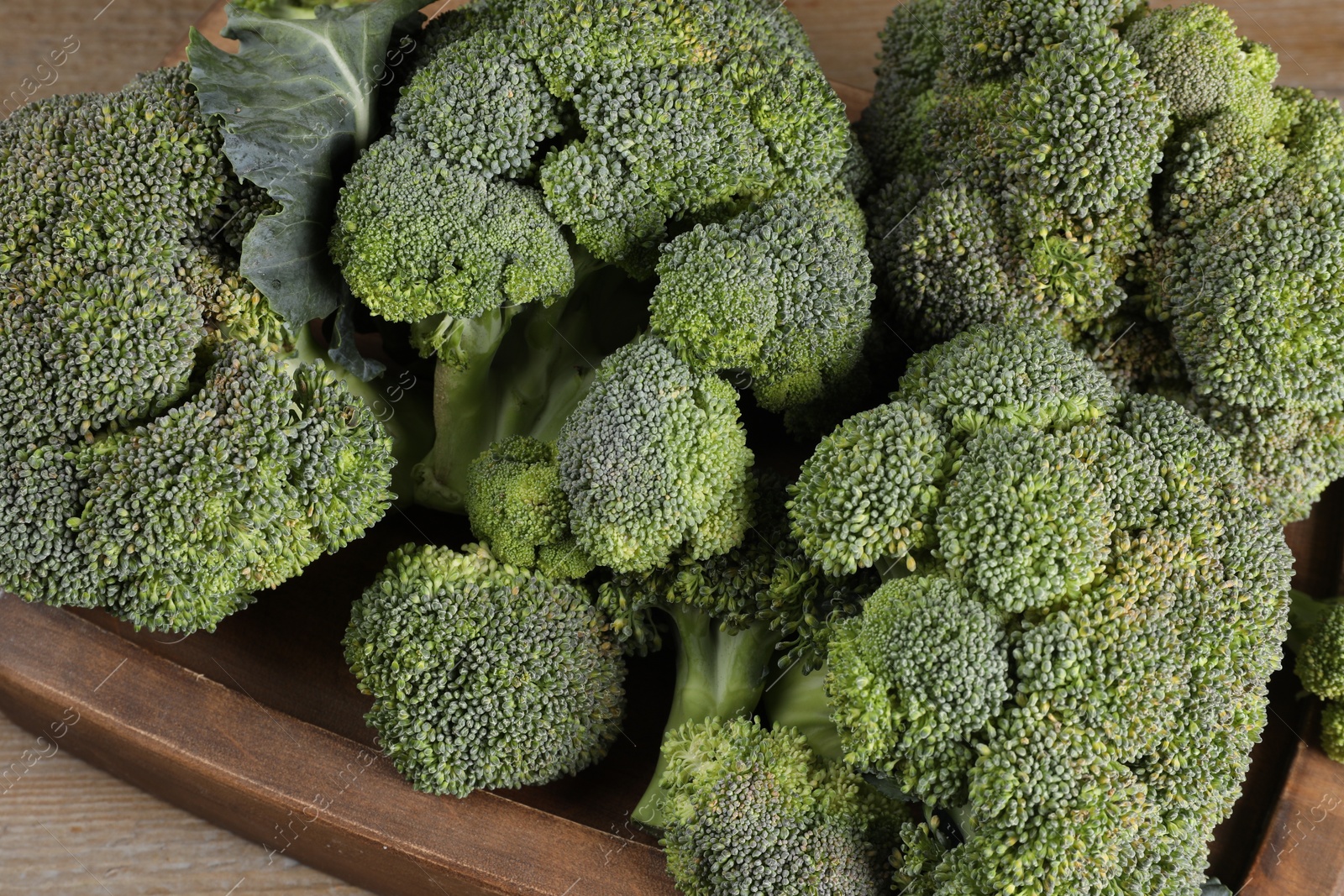 Photo of Tray with fresh raw broccoli on wooden table, closeup