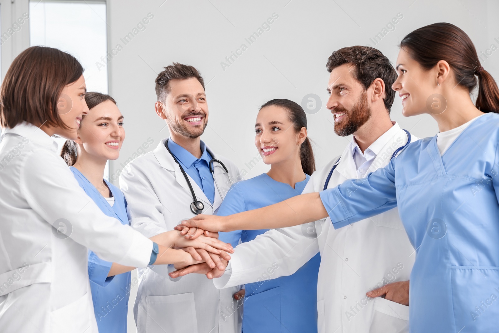 Photo of Team of medical doctors putting hands together indoors