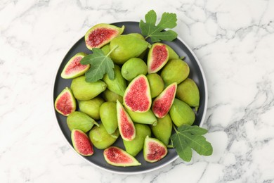 Cut and whole green figs on white marble table, top view