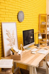 Stylish home office interior with comfortable workplace near yellow brick wall