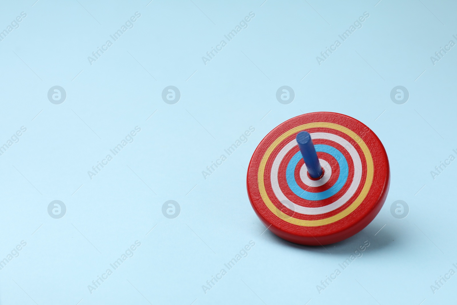 Photo of One colorful spinning top on light blue background, space for text