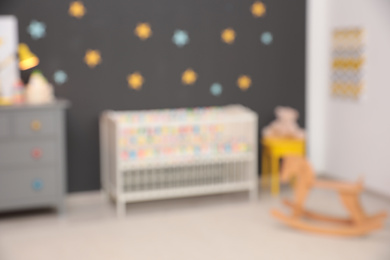 Photo of Blurred view of cute baby room interior with modern crib and rocking horse