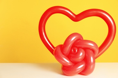 Photo of Rose and heart figures made of modelling balloons on table against color background. Space for text