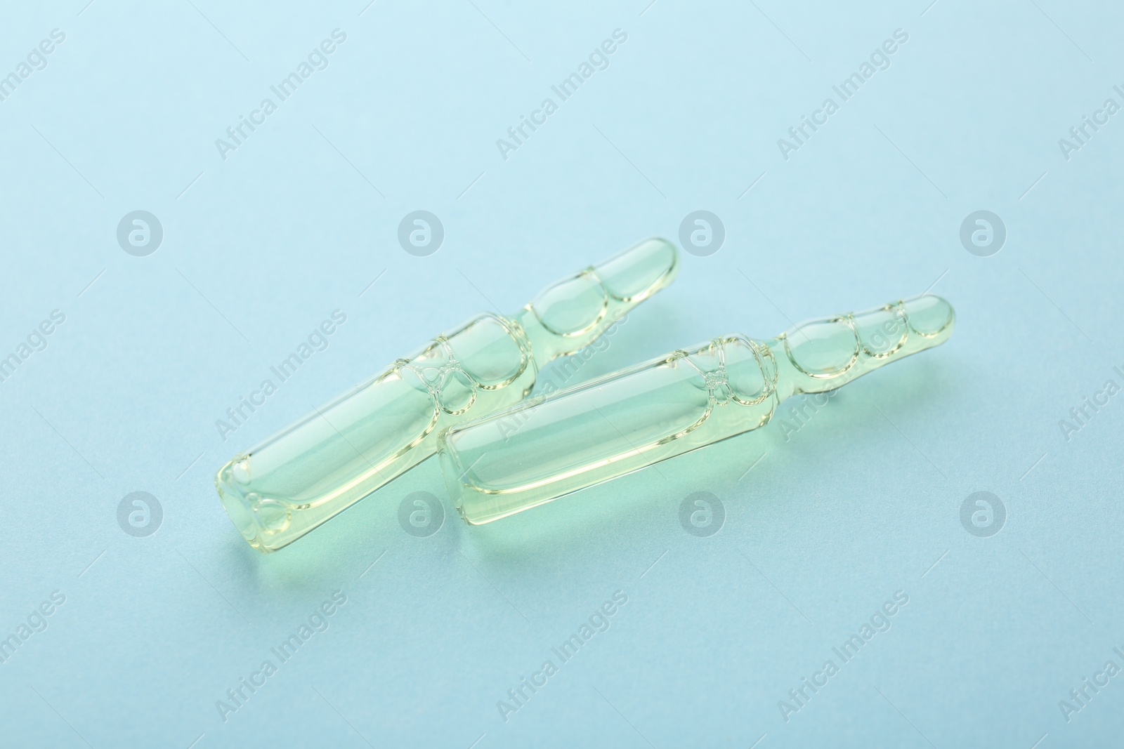 Photo of Glass ampoules with liquid on light blue background