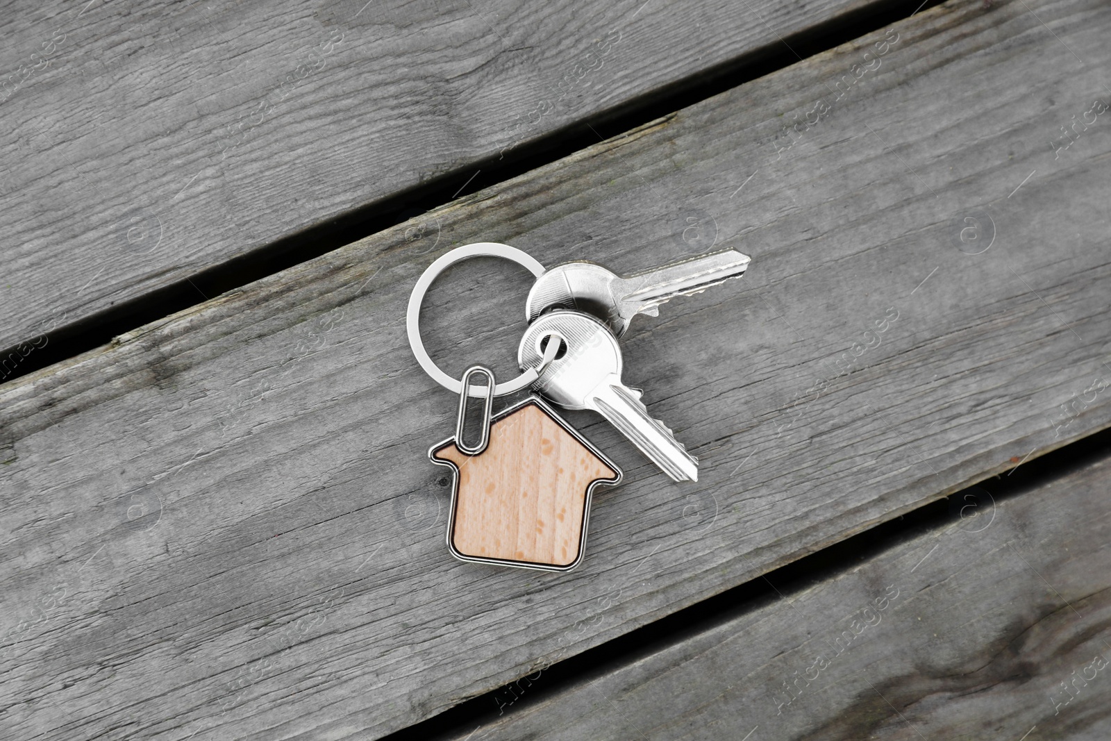 Photo of Keys with trinket in shape of house on wooden table, top view. Real estate agent services