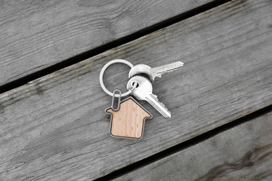 Keys with trinket in shape of house on wooden table, top view. Real estate agent services