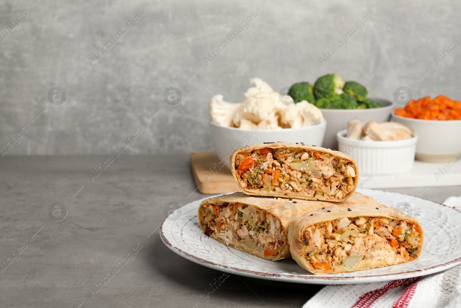 Photo of Pieces of delicious strudel with chicken, vegetables and products on light grey textured table, closeup. Space for text