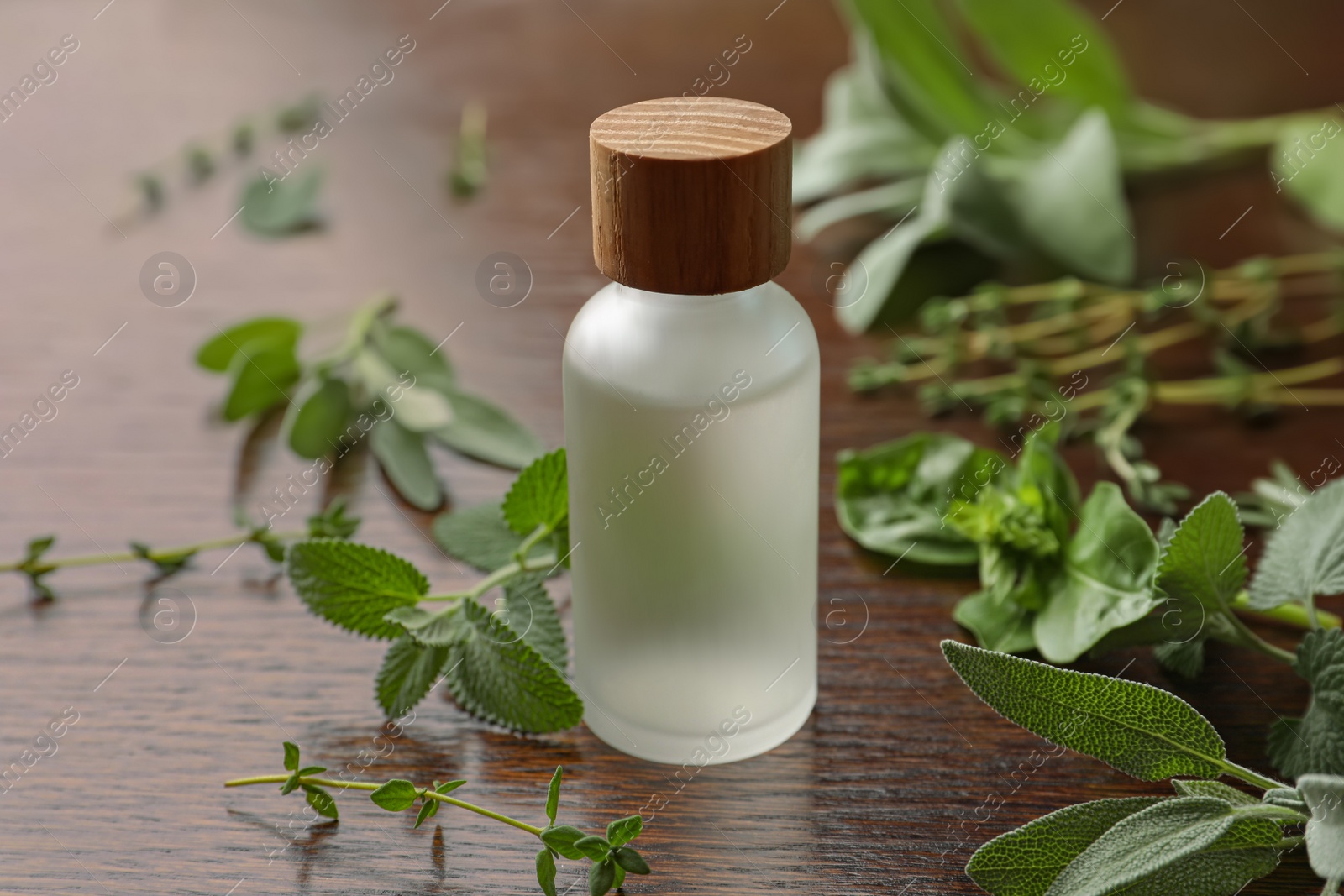 Photo of Bottle of essential oil and fresh herbs on wooden table