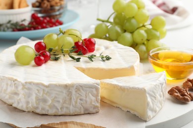 Photo of Brie cheese served with honey and berries on white table, closeup