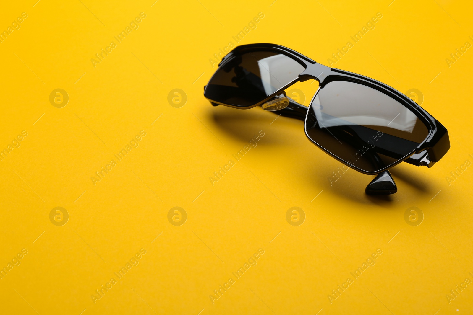 Photo of Stylish sunglasses on yellow background, space for text. Fashionable accessory