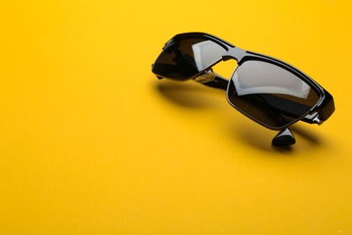 Photo of Stylish sunglasses on yellow background, space for text. Fashionable accessory