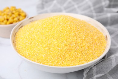 Photo of Raw cornmeal in bowl on white table, closeup