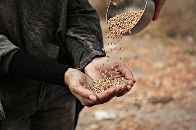 Photo of Woman giving poor homeless person bowl of wheat outdoors, closeup