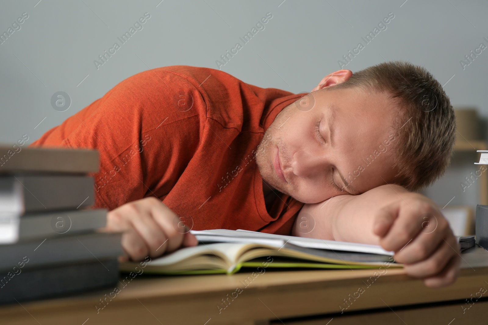 Photo of Tired man sleeping near books at wooden table indoors