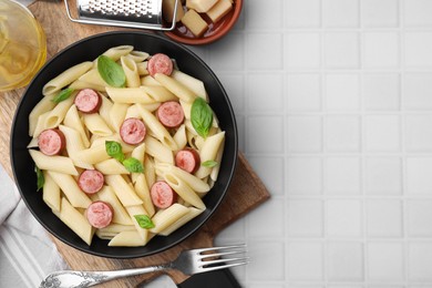 Photo of Tasty pasta with smoked sausage and basil served on white tiled table, flat lay. Space for text