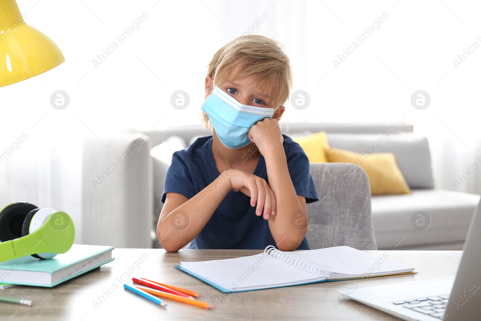Photo of Sad little boy in mask with notebook at home. Distance learning during COVID-19 pandemic