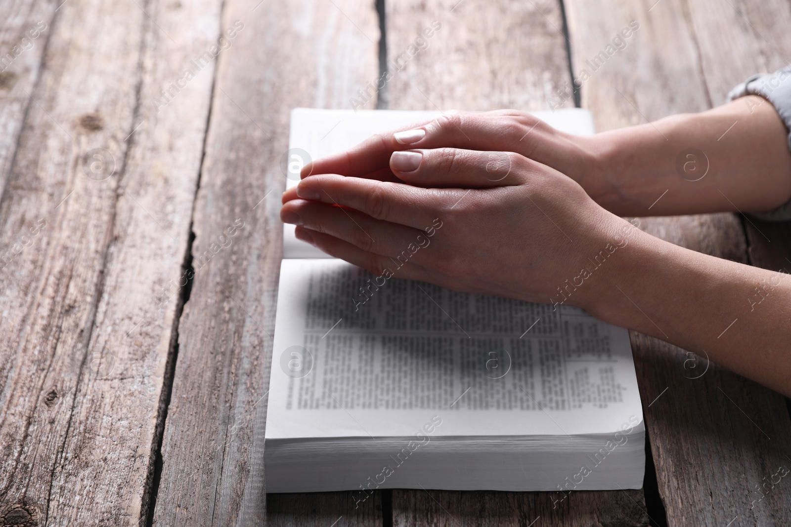 Photo of Religion. Christian woman praying over Bible at wooden table, closeup