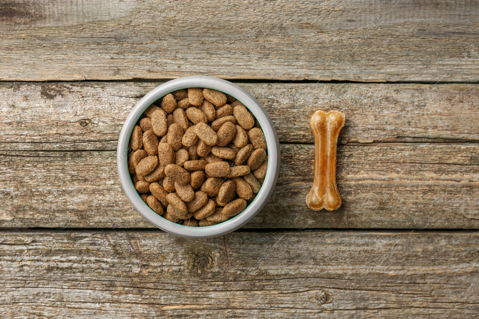 Photo of Dry dog food and treat (chew bone) on wooden floor, flat lay