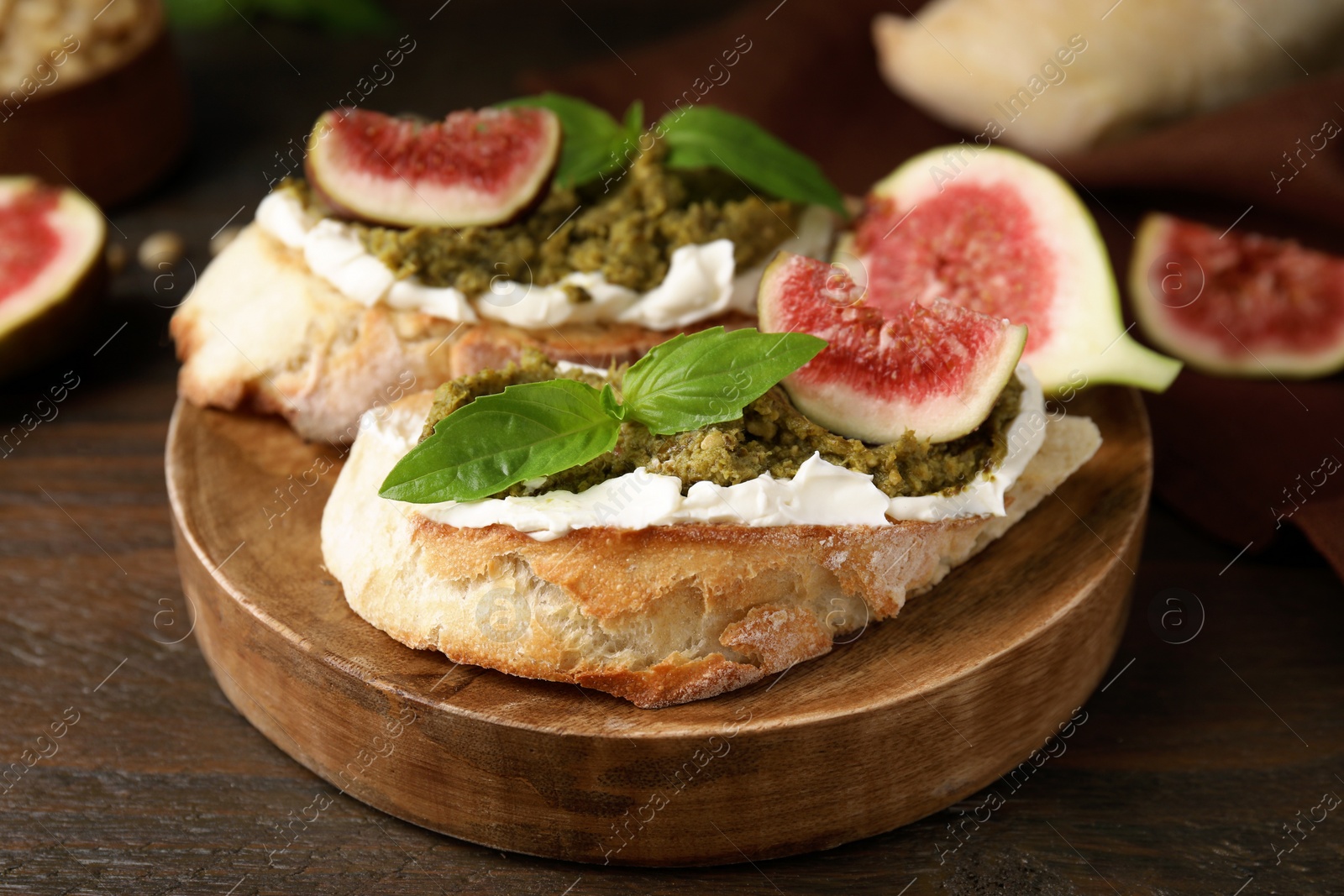 Photo of Tasty bruschettas with cream cheese, pesto sauce, figs and fresh basil served on wooden table, closeup