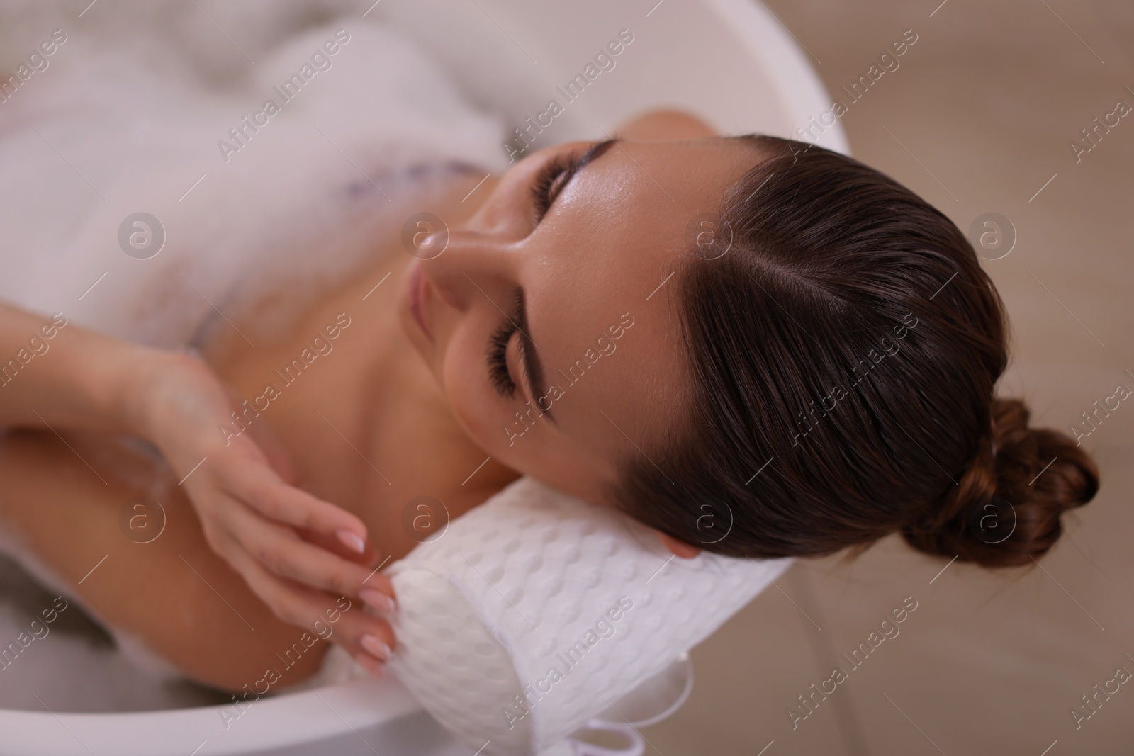 Photo of Young woman using pillow while enjoying bubble bath indoors, above view