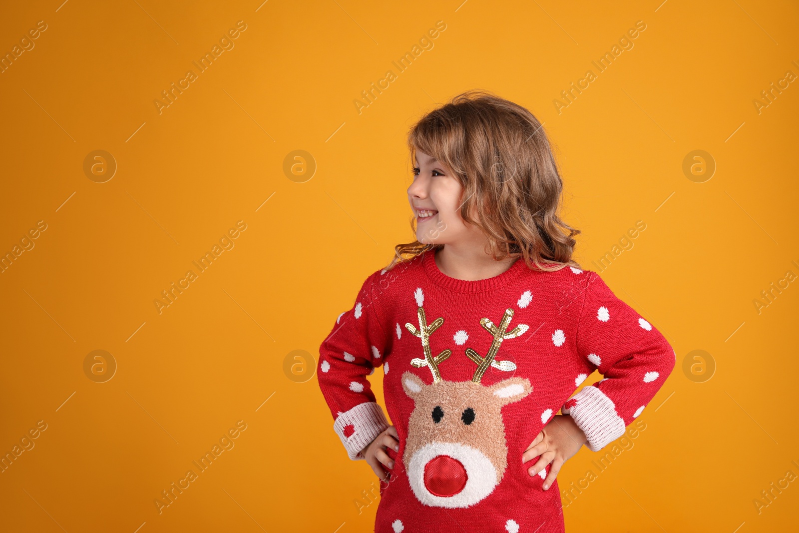 Photo of Cute little girl in red Christmas sweater smiling against orange background. Space for text