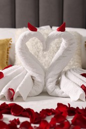 Photo of Honeymoon. Swans made with towels and beautiful rose petals on bed, closeup