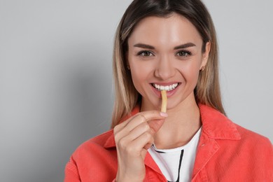 Photo of Young woman eating French fries on grey background, space for text