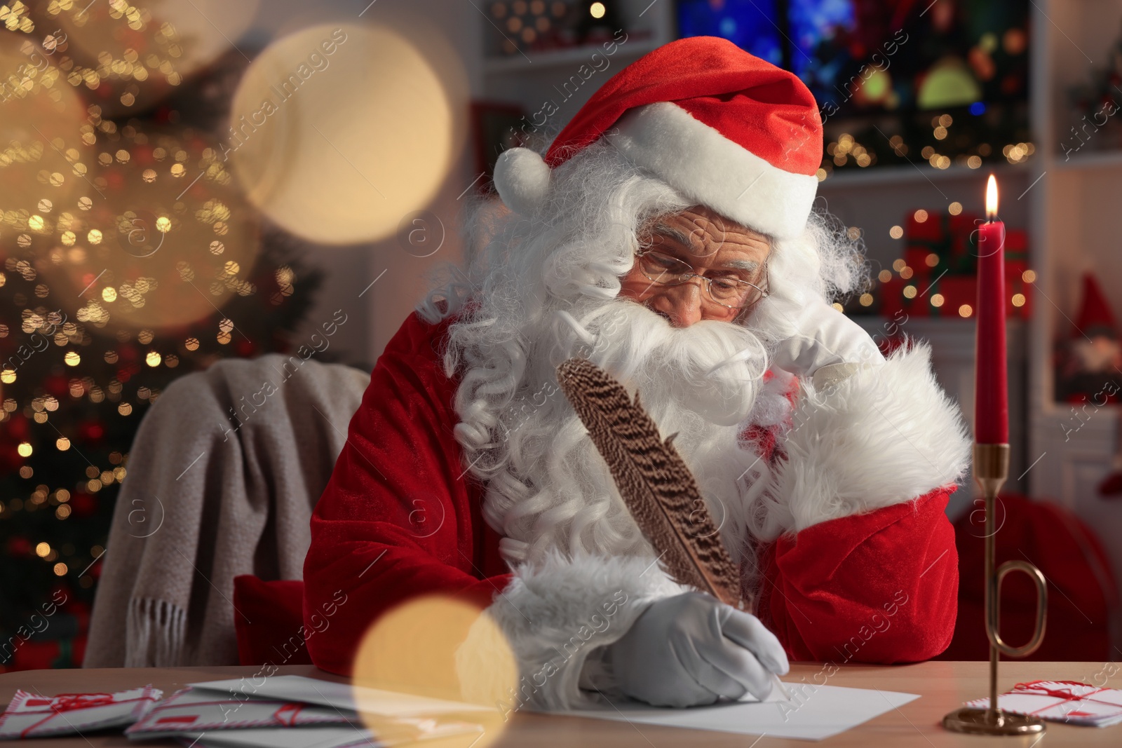 Photo of Santa Claus writing letter at table in room decorated for Christmas