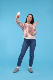 Photo of Smiling young woman taking selfie with smartphone on light blue background