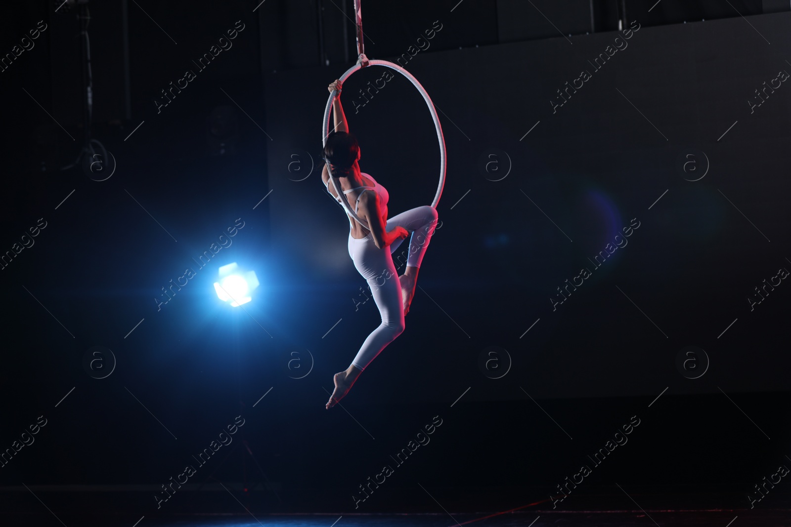 Photo of Young woman performing acrobatic element on aerial ring against dark background